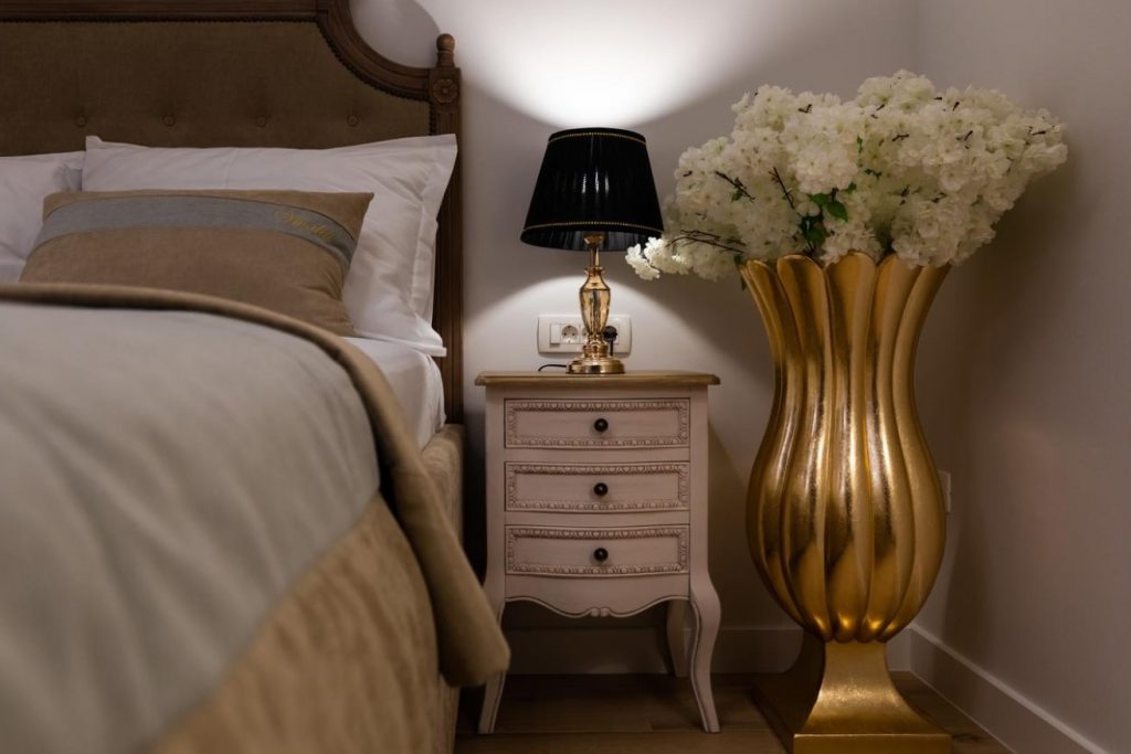 noćni ormarić pored kreveta i velike zlatne vaze sa cvijećem